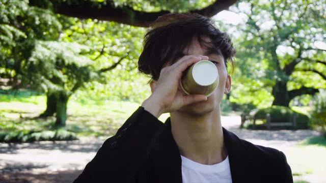 Young Japanese Business Man Wearing Suit Drinking Coffee While Walking in Park