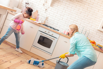 Cute helpful girl assisting her mother with cleaning the kitchen