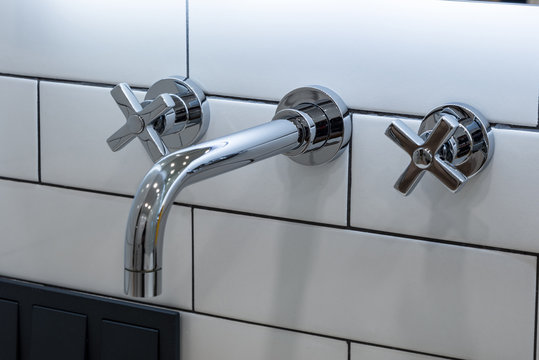 Chrome plated faucet with two knobs sticking out of the wall
