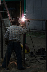 Welder is welding metal part in playground. A man in a protective mask welds a horizontal bar for workout. Welding process