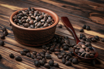 Inshell pine nuts in a bowl and wooden spoon and scattered on a wooden table