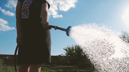 Diligent woman in panama watering her garden on a sunny day in slow motion