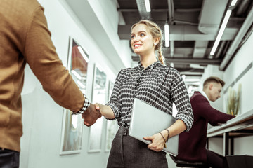 Blonde positive woman with wide smile carrying closed laptop