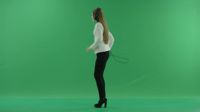 Happy businesswoman listening to music in the headphones and dancing on the spot. She wears formal dress: white shirt and blak trousers, standing in the centre the greenscreen