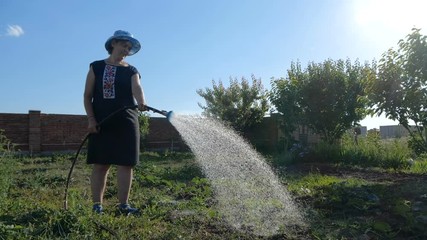 Funny woman in panama watering her garden from a shower nozzle in slo-mo