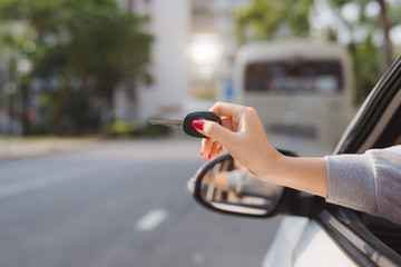 Woman holding the ignition keys of a car in her hand dangling them through the open side window