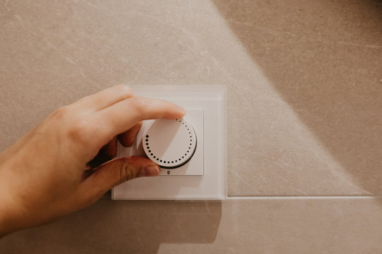 Saving energy concept: Human hand turning down electrical light dimmer switch