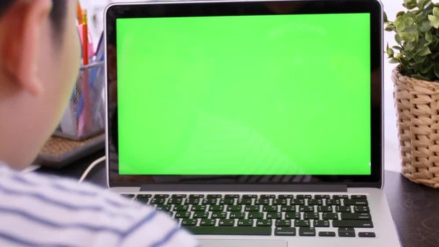 Over the shoulder shot of Asian boy looking at green screen. Office person using laptop computer with laptop green screen, 4K Zoom in dolly shot