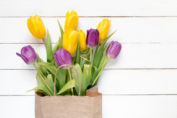Yellow and purple flowers tulips in a paper bag on a white wooden background, a festive spring background greeting card