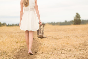 Young woman walking on path holding boots