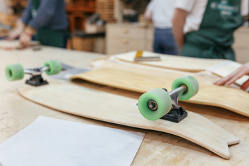Unidentified craftsmen create wooden skateboard lying on a table in a carpentry workshop. Concept...