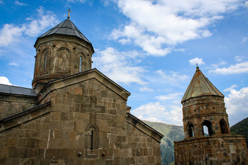 Fototapeta na wymiar Gergeti Trinity Church in Georgia, Stepantsminda, Kazbegi. Orthodoxy, Christianity, religion, cross. Blue sky. 