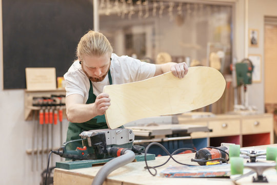 Scandinavian hipster joiner makes a skateboard and polishes the board with a professional grinding machine. Concept of man at work on wood - Powered by Adobe