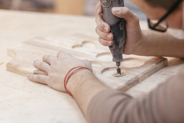 Hands of a professional carpenter make a souvenir kitchen board with a tool with a cutter. Concept...