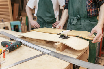 Hands of a male carpenter and his student make a skateboard on the table in his carpentry workshop. Wooden products concept