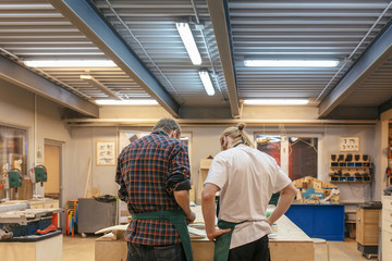 Rear view two carpenters working on a new wooden product in their spacious workshop. Concept of creation of unique wooden products