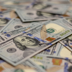 Macro shot of Benjamin Franklin's portrait on a new 100 dollar US money note, with defocused background of many more identical money notes in a mess.