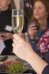 Woman is drinking white wine and having rest with her friends. Close-up of woman s hands holding glass