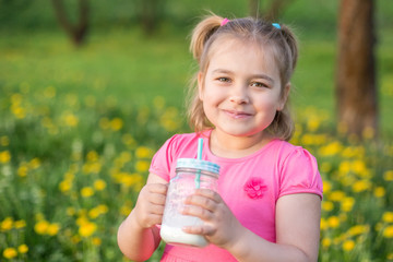 Positive smiling cute blondie girl laughing and drinking milk outdoors in green garden in blossom