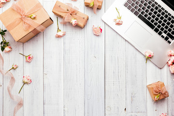 Workspace with a laptop keyboard, rose flowers, gift boxes wrapped in kraft paper on wooden background. Copy space for text,  Top view, flat lay. 