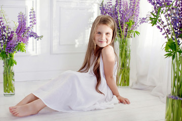 Obraz na płótnie Canvas Beautiful little emotional girl siting among violet flowers. A flower decor in an interior
