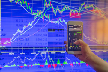 business hand hold and touch screen on smartphone or cellphone over blur stock chart market monitor background,business stock concept