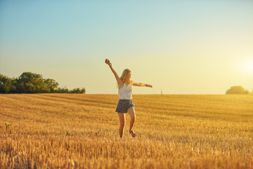 Naklejka na ściany i meble Cute young woman jumping in a wheat field.