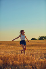 Cute young woman jumping in a wheat field.