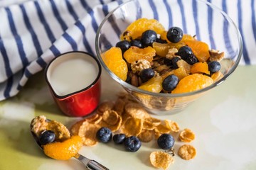 Healthy breakfast with blueberries , tangerines , corn flakes,  and milk on the colored bachground .