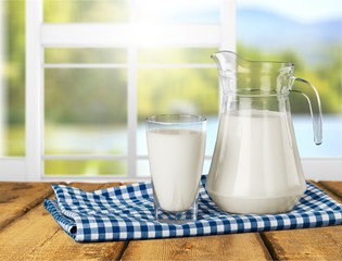 Glass of milk and jar on table with cloth and background