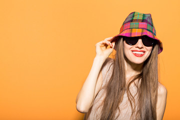  Happy young beautiful woman wearing sunglasses and hat over bright orange background