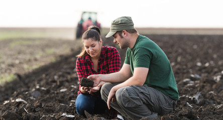 Young farmers exam dirt while tractor is plowing field