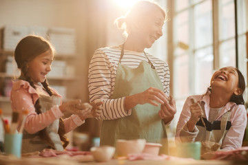 Waist up portrait of art teacher having fun with kids in pottery class , scene lit by sunlight
