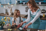Happy mother and daughter coloring eggs at home