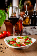 Concept of Italian cuisine. Caprese salad with cherry tomatoes, arugula and basil salad mix, and mozzarella cheese. Serving dishes in white plate in a restaurant. background image.