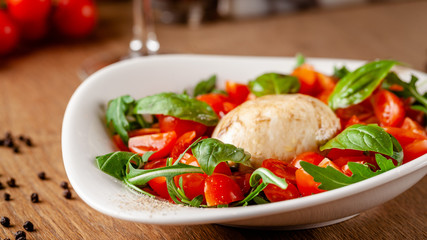 Concept of Italian cuisine. Caprese salad with cherry tomatoes, arugula and basil salad mix, and mozzarella cheese. Serving dishes in white plate in a restaurant. background image.