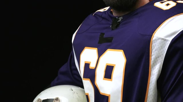 American football player holding a head gear against black background