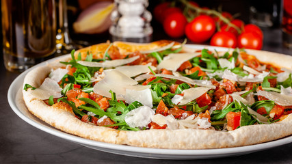 Concept of Italian cuisine. Thin pizza with thick sides with salmon, arugula and cherry tomatoes and parmesan cheese. The chef fills the pizza with garlic oil. Background image.