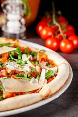 Concept of Italian cuisine. Thin pizza with thick sides with salmon, arugula and cherry tomatoes and parmesan cheese. The chef fills the pizza with garlic oil. Background image.