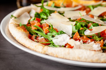 Concept of Italian cuisine. Thin pizza with thick sides with salmon, arugula and cherry tomatoes and parmesan cheese. The chef fills the pizza with garlic oil. Background image.