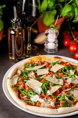  Concept van de Italiaanse keuken. Dunne pizza met dikke zijkanten met zalm, rucola en cherrytomaatjes en Parmezaanse kaas. De chef vult de pizza met knoflookolie. Achtergrond afbeelding. © zukamilov