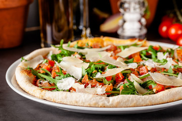 Concept of Italian cuisine. Thin pizza with thick sides with salmon, arugula and cherry tomatoes and parmesan cheese. The chef fills the pizza with garlic oil. Background image.