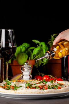 Concept of Italian cuisine. Thin pizza with thick sides with salmon, arugula and cherry tomatoes and parmesan cheese. The chef fills the pizza with garlic oil. Background image.