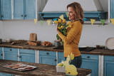 Happy young woman with yellow tulips on kitchen