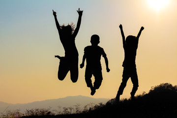 Silhouette of happy children jumping playing on mountain meadow at sunset time