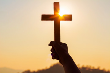 human hands praying to the GOD while holding a crucifix symbol with bright sunbeam on the sky