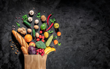 Healthy food in full paper bag of different products vegetables and fruits on dark background