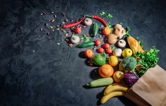 Healthy food in full paper bag of different products vegetables and fruits on dark background