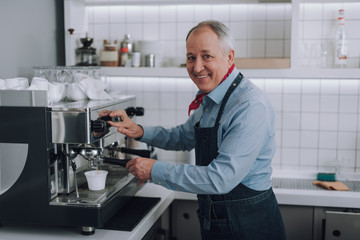 Joyful old man making fresh coffee with professional coffee machine