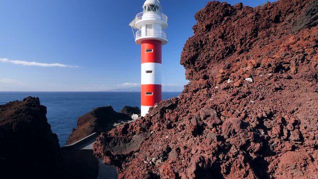 Pedestal view of a lighthouse located in a volcanic cliff in Punta de Teno, Tenerife (Canary Islands), in the background the isle of La Gomera